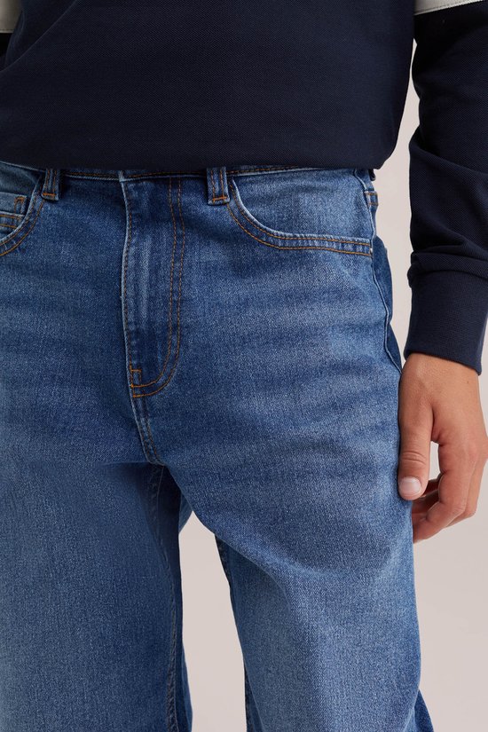 Blauwe loose fit spijkerbroek met oranje stiksels, gesp, en zakken, gedragen door een jongen.