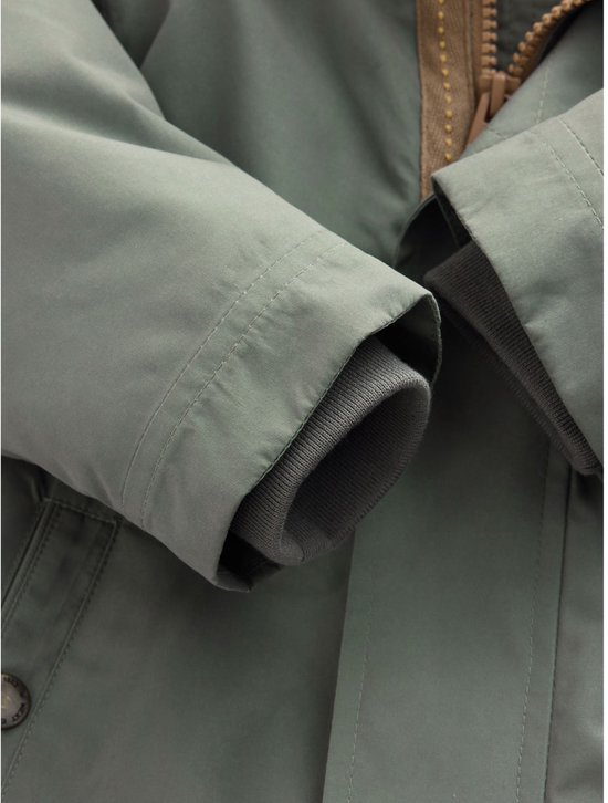 Detailopname van de mouwen van de groene parka, afgewerkt met grijze geribbelde boorden.
