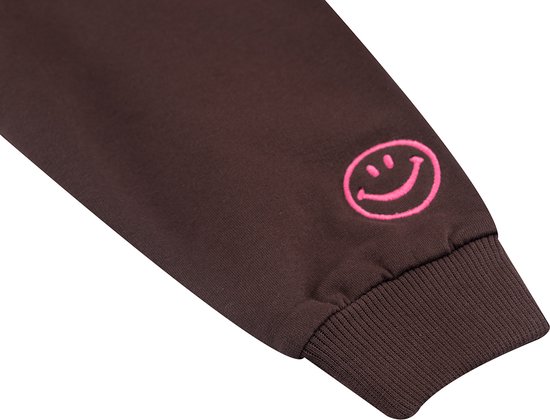 Detail van de mouw van een bruine sweater met een felroze lachende smiley.
