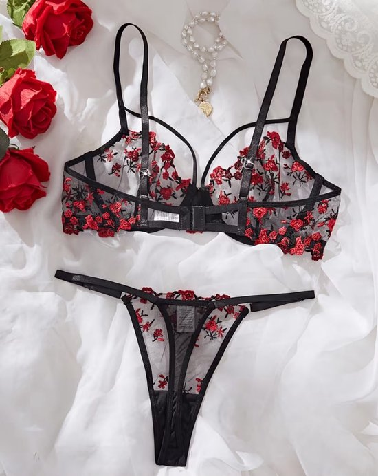 Zwarte kanten lingerie set met rode bloemen. BH en bijpassende string. Ketting met parels ligt ernaast.