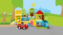 Glissière bleue avec château jaune, une voiture rouge avec un enfant, un arbre avec une figurine et une maisonnette avec un chien.