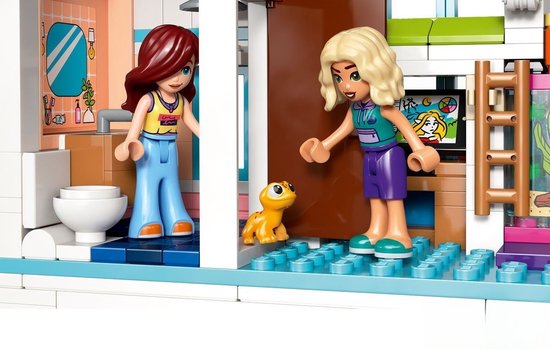 Twee LEGO Friends poppetjes, één in een geel topje en blauwe broek, de ander in een turquoise topje en paarse broek, staan met een klein geel beestje.