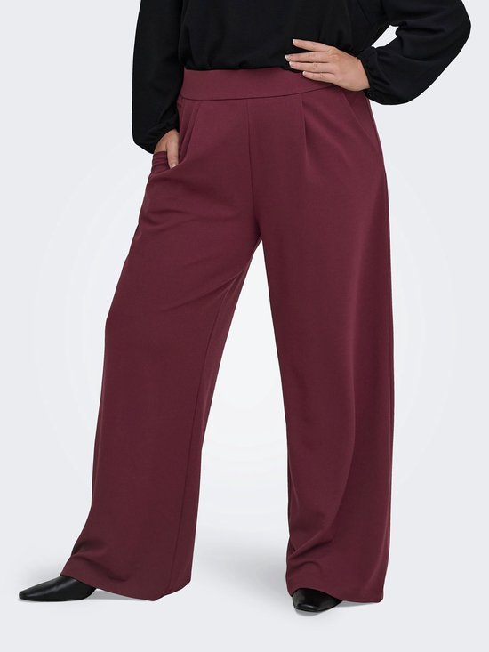 Vrouw met zwarte top en bordeauxrode wijde broek met plooien, van voren gezien.