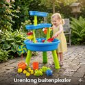 Een lachend meisje speelt met een blauwe en groene watertafel in de tuin.