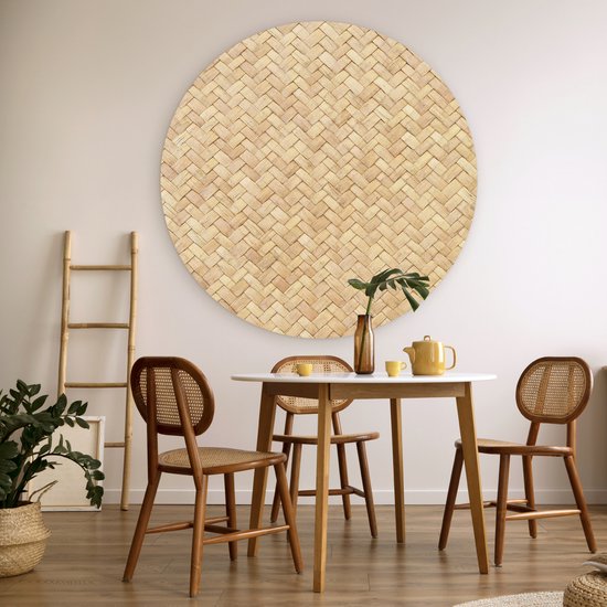 Décoration murale ronde en rotin avec motif tressé, au-dessus d'une table blanche avec des chaises en bois.