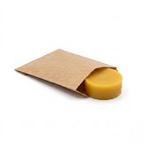 Een geel bijenwasblok half in een bruin papieren zakje op een witte achtergrond.