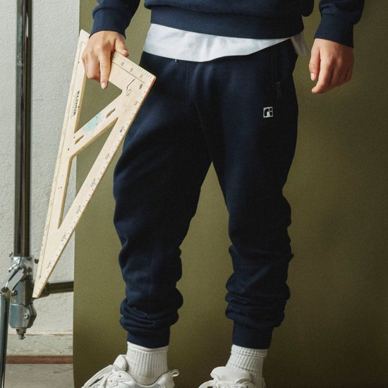 Jongen in donkerblauwe joggingbroek met een wit T-shirt, witte sokken en sportschoenen.