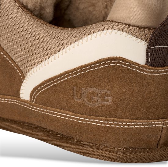 Detail van bruine UGG-sneaker met beige en witte biezen en UGG-logo.