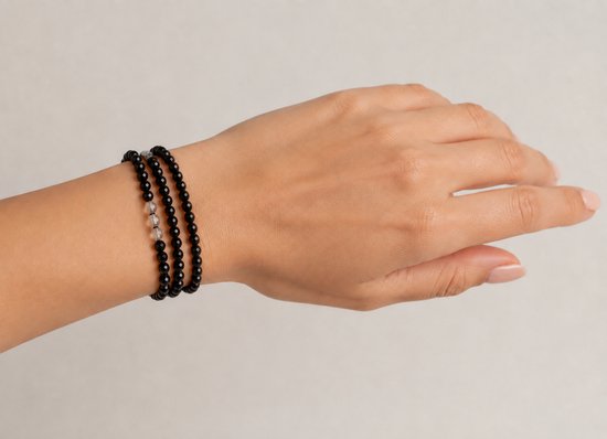 Drie elastische armbanden, twee met zwarte kralen en één met een transparante kraal, gedragen om een pols.