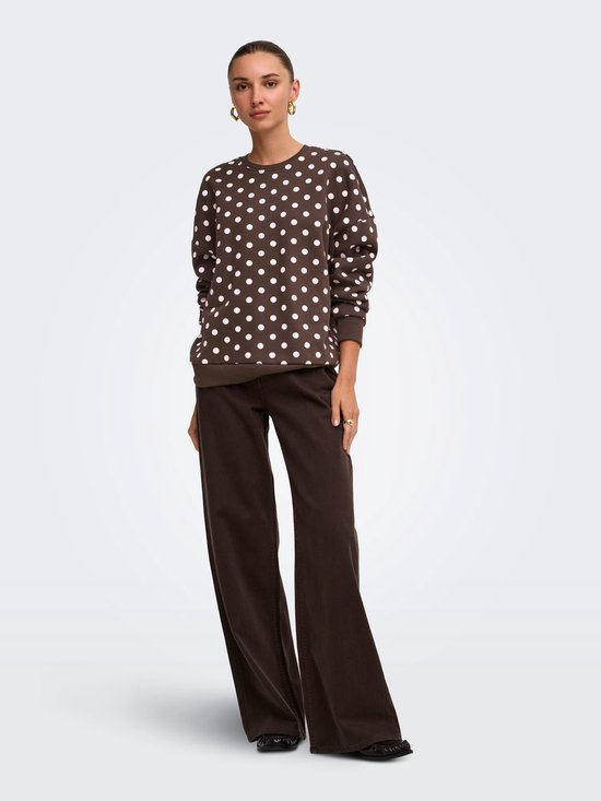 Model draagt een bruine sweater met witte polkadots, gecombineerd met een bruine broek.