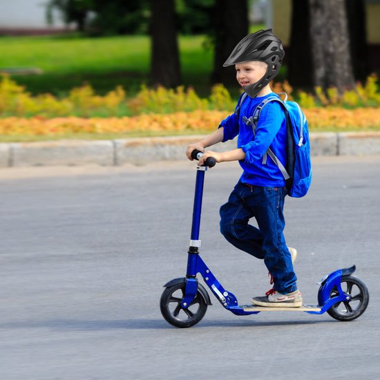 Jongen in blauw shirt en rugzak draagt een zwarte helm en rijdt op een blauwe step.