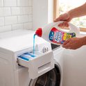 Handen gieten blauw Color Reus vloeibaar wasmiddel in een wasmachinelade. Wit aanrecht en witte wasmachine.