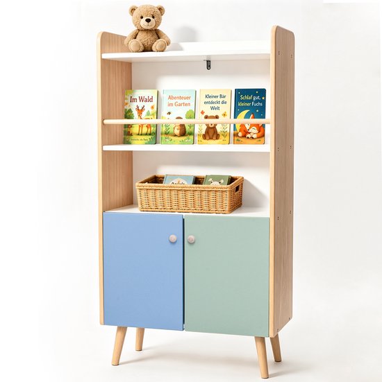 Een witte ALVIX kinderboekenkast met houten poten, blauwe en groene deuren, gevuld met boeken en speelgoed.