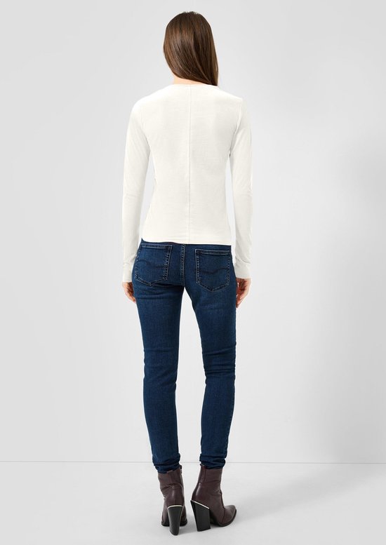 Model van achteren met een witte longsleeve, donkerblauwe skinny jeans en bruine enkellaarsjes.