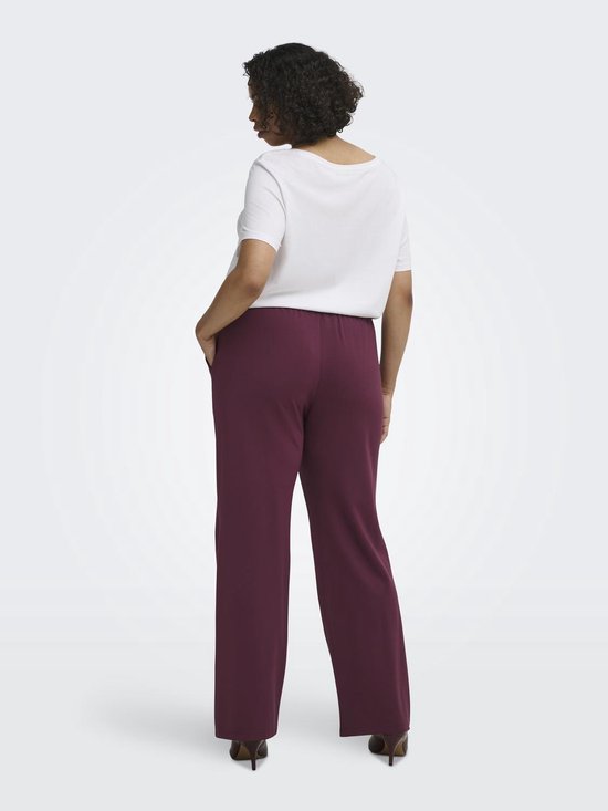 Model met lange bordeauxrode broek met rechte pijpen, witte top en hakken.