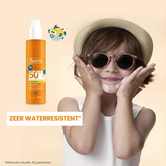 Een jong kind met een hoed en zonnebril, met zonnebrandcrème op de wangen, naast een oranje flacon zonnebrandspray SPF 50+ en een cartoonvis.