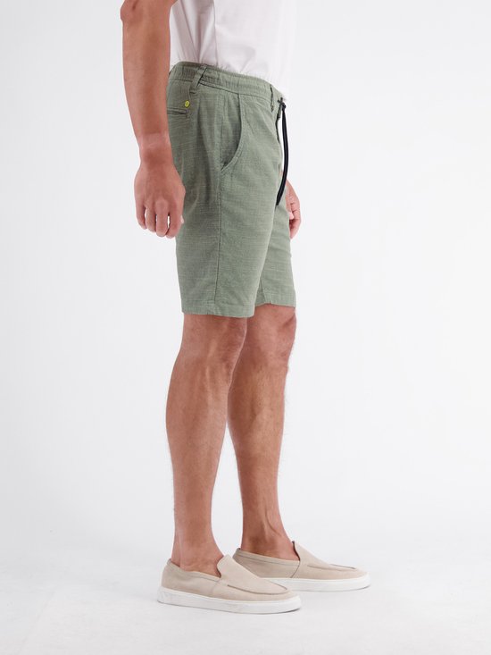 Man met groene chino shorts met trekkoord, staand in een witte polo.