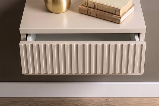 Beige hangend nachtkastje met open lade en verticale ribbels op het front, naast een bed.