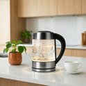 Glazen waterkoker met RVS, met sfeervolle verlichting en een kopje thee.