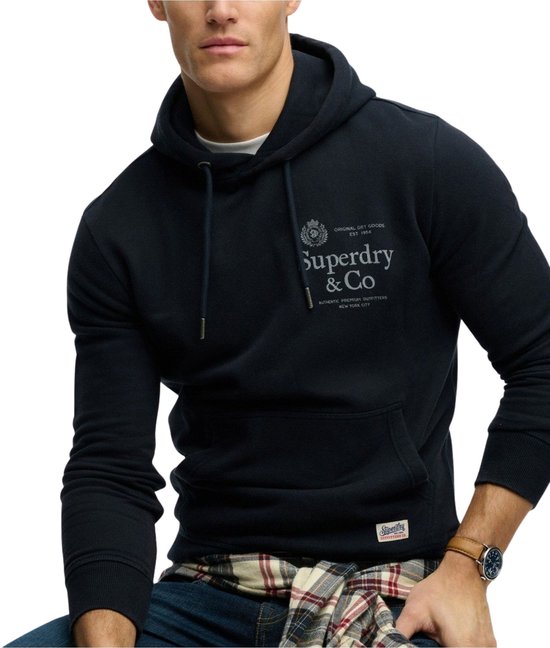 Model in donkerblauwe hoodie met geruit overhemd om middel geknoopt.