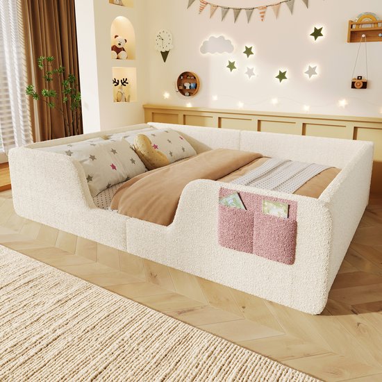 Laag kinderbed van lichtbeige teddy stof met roze opbergvakjes, opgemaakt met beddengoed.