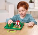 Jongen met rood haar speelt met Roodkapje-bordspel. Bevat Roodkapje, wolf, huisje en bomen.