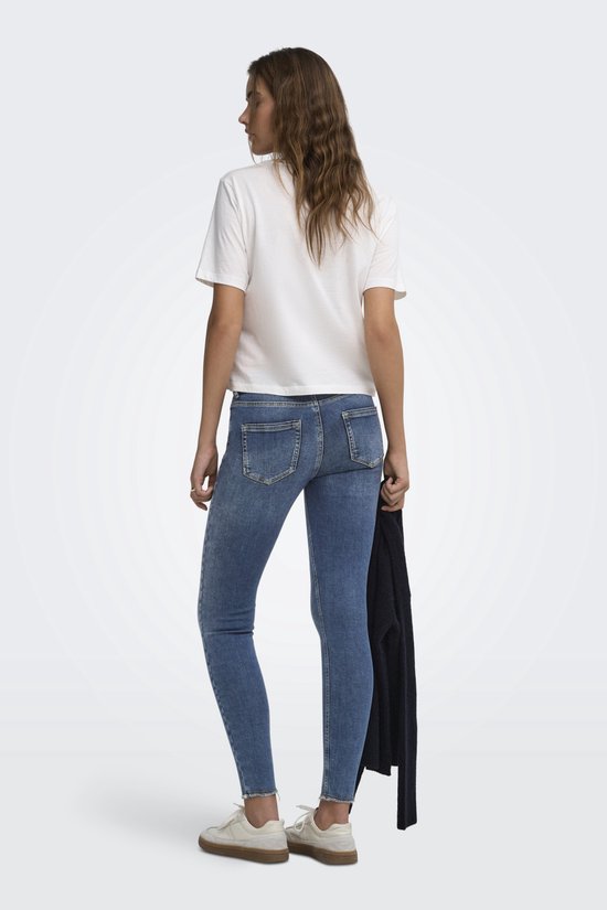 Vrouw in blauwe skinny jeans met lichte wassing, rafelige zoom en witte top.