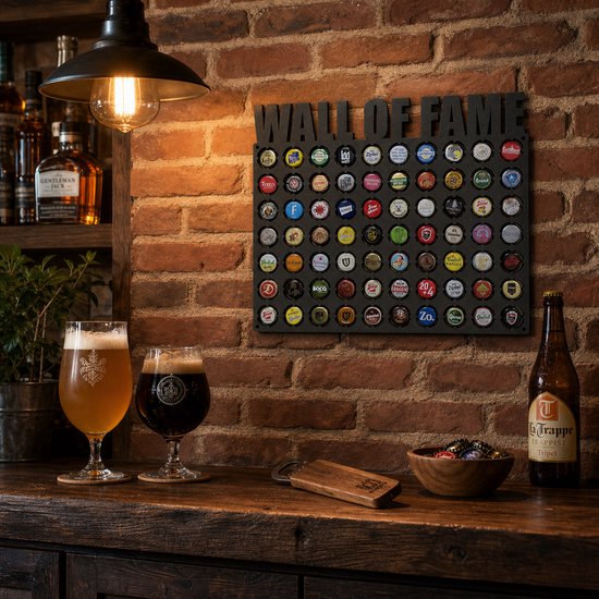Donkergrijze bierdoppenbord met de tekst 'WALL OF FAME' bovenkant. Hieronder 5 rijen met bierdoppen. Twee glazen bier, een fles La Trappe Tripel en een houten kom met doppen op de voorgrond.