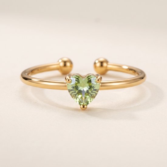 Gouden ring met een lichtgroene hartvormige steen op een crèmekleurige achtergrond.