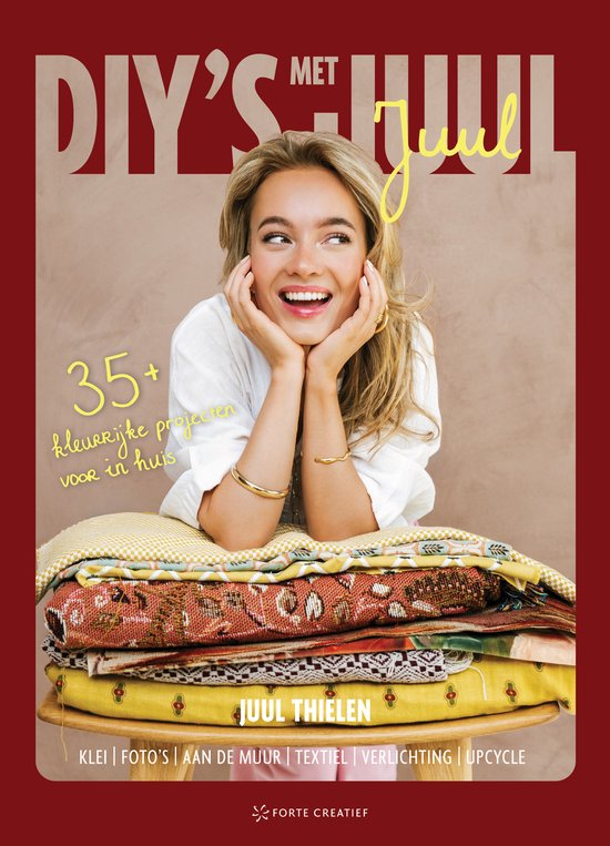 Vrolijke vrouw met blonde haren, zittend op een stapel kleurrijk textiel. Titel: DIY's met Juul.