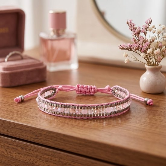 Roze geweven armband met facet geslepen glaskralen en kleine roze kralen, aan een verstelbaar koord. Op een houten tafel.