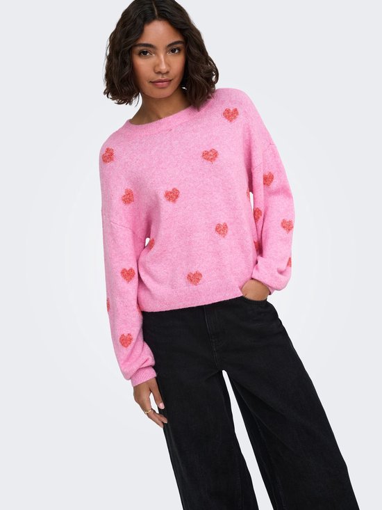 Model in roze trui met all-over rode hartjesprint en zwarte jeans.