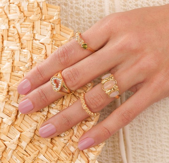 Dameshand met nagels in lichtroze nagellak, draagt meerdere gouden ringen met diverse edelstenen.