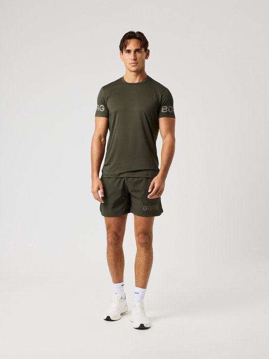 Man staat in een donkergroene sportoutfit: t-shirt met korte mouwen en korte broek, beide met grijze logo opdruk.