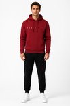 Man staand in bordeauxrode hoodie met 'PARIS'-print en zwarte joggingbroek met 'PARIS'-print.