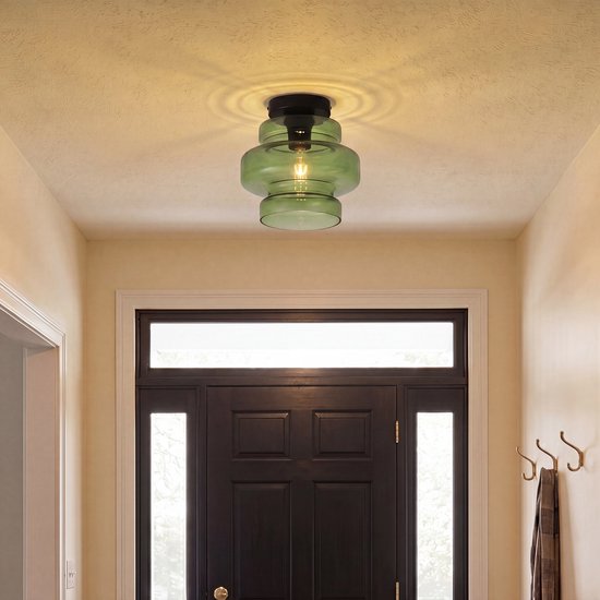 Groene glazen plafondlamp in een hal bij een zwarte deur, met licht dat zich naar het plafond verspreidt.