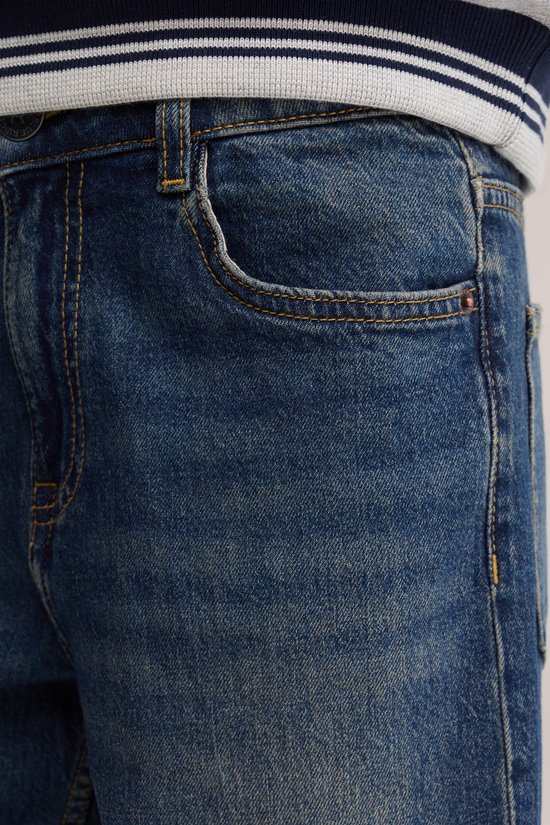 Close-up van de zak van een donkerblauwe jeans, gedragen met een gestreepte trui.