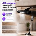 Zwarte steelstofzuiger met LED-koplamp die vuil zichtbaar maakt onder een bank en op tapijt.