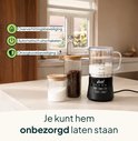 Zwarte melkopschuimer met glazen kan, met oververhittings- en droogkookbeveiliging, naast potten met koffiebonen en suiker.