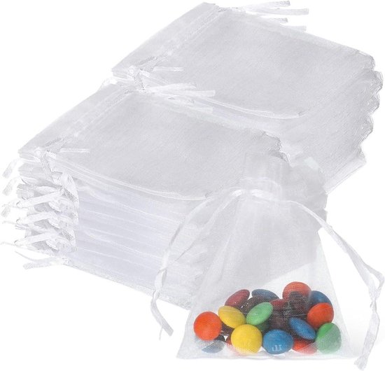 Une pile de pochettes blanches en organza à cordon, avec une seule pochette remplie de bonbons colorés.