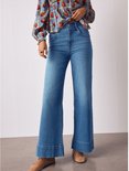 Onderlichaam van een model in een blauwe top met appelprint en gele ruit, met een hoge taille en wijde jeans.