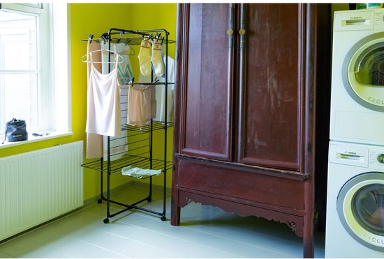 Zwarte droogtoren met lichtroze kledingstukken en handdoeken in een woonkamer met een gele muur en een houten kast.