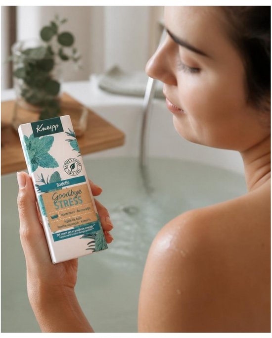 Vrouw in bad houdt een fles Kneipp Goodbye Stress badolie met watermunt en rozemarijn vast.