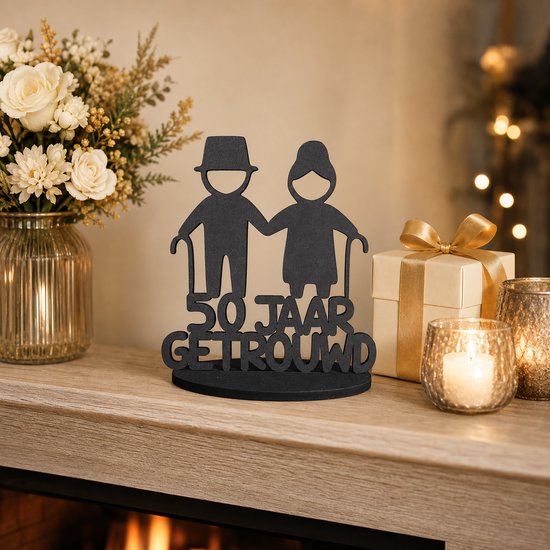 Zwart decoratiebord met twee silhouetten van een ouder echtpaar met wandelstokken en de tekst '50 JAAR GETROUWD', bij kaarsen en een cadeau.