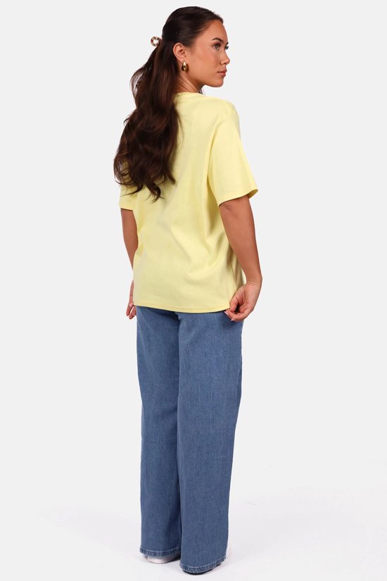 Zijaanzicht van een model in een lichtgele oversized T-shirt en blauwe spijkerbroek.