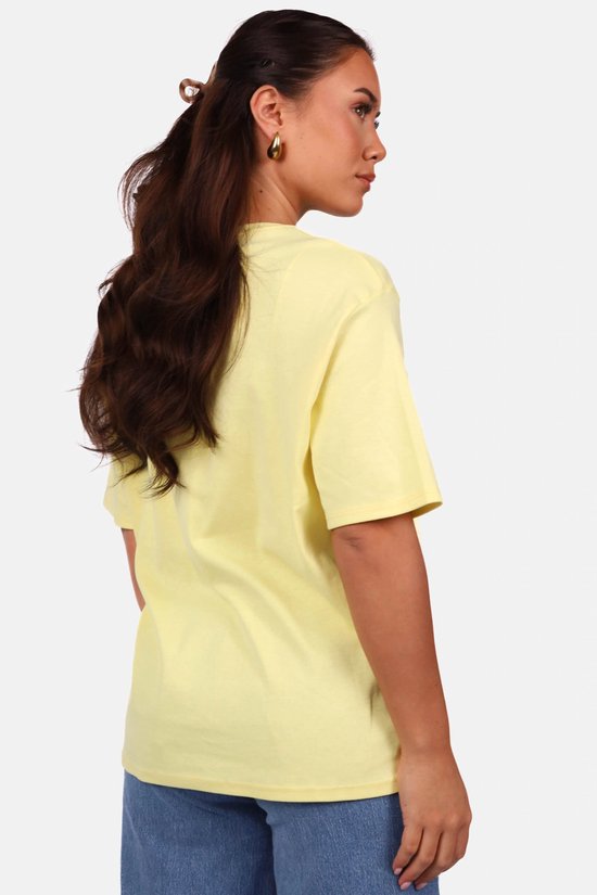 Zijaanzicht van een model dat een lichtgele oversized T-shirt en blauwe jeans draagt.
