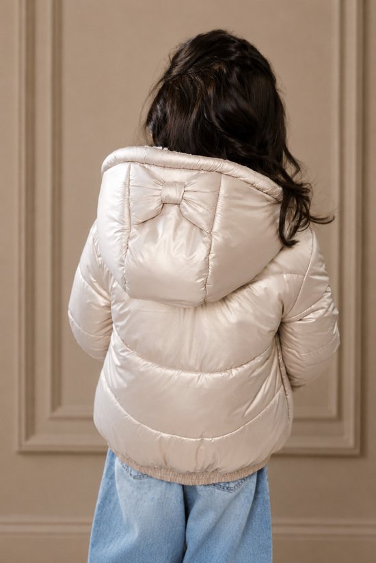 Meisje draagt goudkleurige winterjas met strik op de capuchon, denim spijkerbroek.