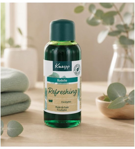 Kneipp Badolie Refreshing Eucalyptus in fles met donkergroene dop. Het etiket toont "Badolie Refreshing Eucalyptus". Naast de fles liggen groene handdoeken en een klein houten schaaltje met eucalyptusblaadjes.