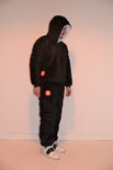 Zwarte oversized hoodie en joggingbroek met rode 'S' logo's. Model draagt witte sneakers.