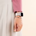 Een pols met een zilverkleurig stalen bandje om een smartwatch. Een roze trui en beige rok worden gedragen.